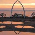 Whale bones arch in front of setting sun and ocean.